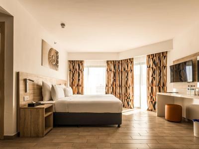 Helles Hotelzimmer mit großem Bett, Vorhängen und moderner Einrichtung.