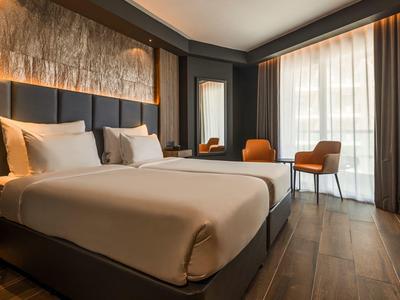 Modernes Hotelzimmer mit großem Bett, Holzfußboden und bodentiefen Fenstern mit Vorhängen.