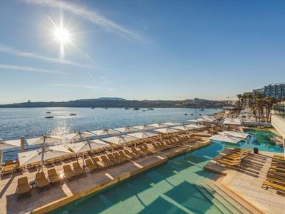 Spiaggia soleggiata con lettini, ombrelloni e acqua limpida accanto a un hotel.