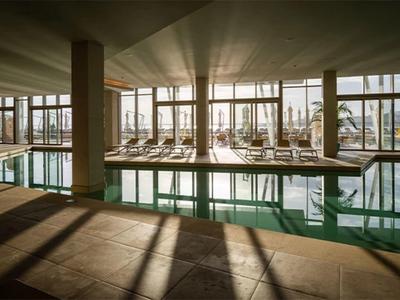 Innenpool mit Liegestühlen und großen Fenstern, durch die Sonnenlicht strömt.