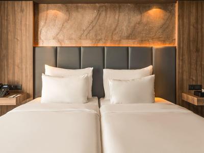 Modernes Hotelzimmer mit zwei Einzelbetten, Holzverkleidung und warmem Licht.