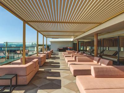 Lounge sulla terrazza con divani rosa e soffitto in legno, vista sulla città di giorno.