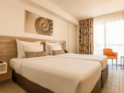 Hell eingerichtetes Hotelzimmer mit Doppelbett, Holzdekor und Fenster mit Vorhängen.