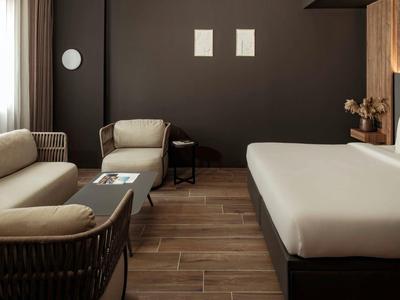 Modernes Hotelzimmer mit bequemen Sitzmöbeln, großem Bett und dunkler Wandgestaltung.