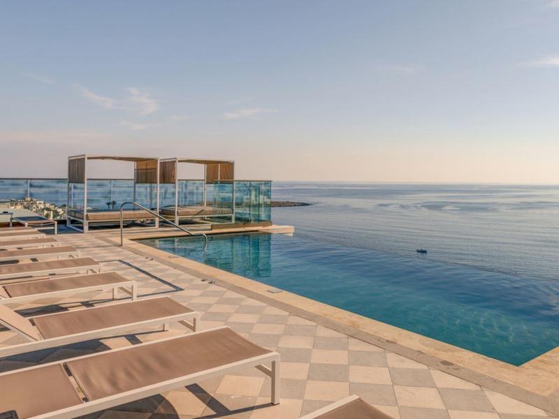 Infinity-Pool mit Liegestühlen und Blick auf das Meer bei Sonnenuntergang.