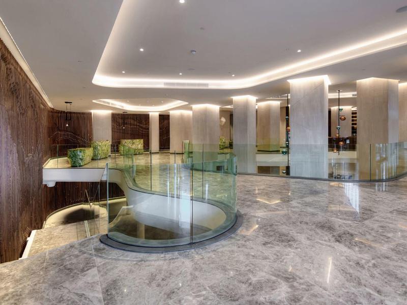 Moderner Hotellobby mit Marmorfußboden, geschwungenem Glasgeländer und warmen Beleuchtungselementen.