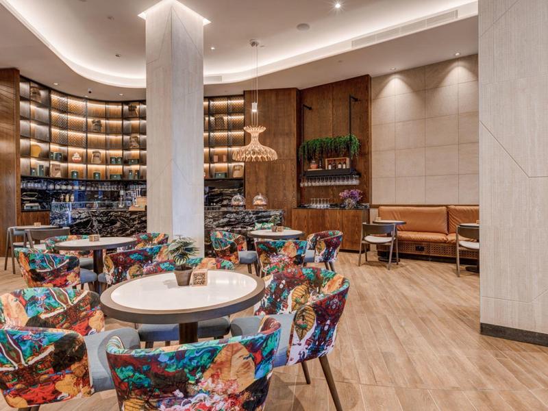 Moderne Hotellounge mit bunten Sesseln, runden Tischen und dekorativem Bücherregal an der Wand.