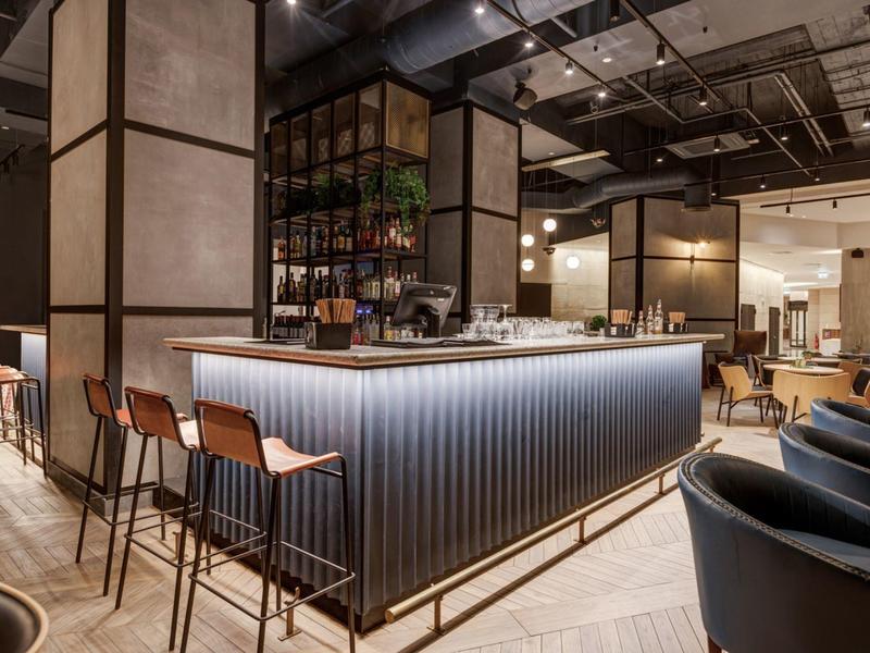 Moderner Hotelbarbereich mit beleuchtetem Tresen und hohen Stühlen in warmem Licht.