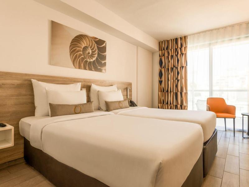 Hell eingerichtetes Hotelzimmer mit Doppelbett, Holzdekor und Fenster mit Vorhängen.