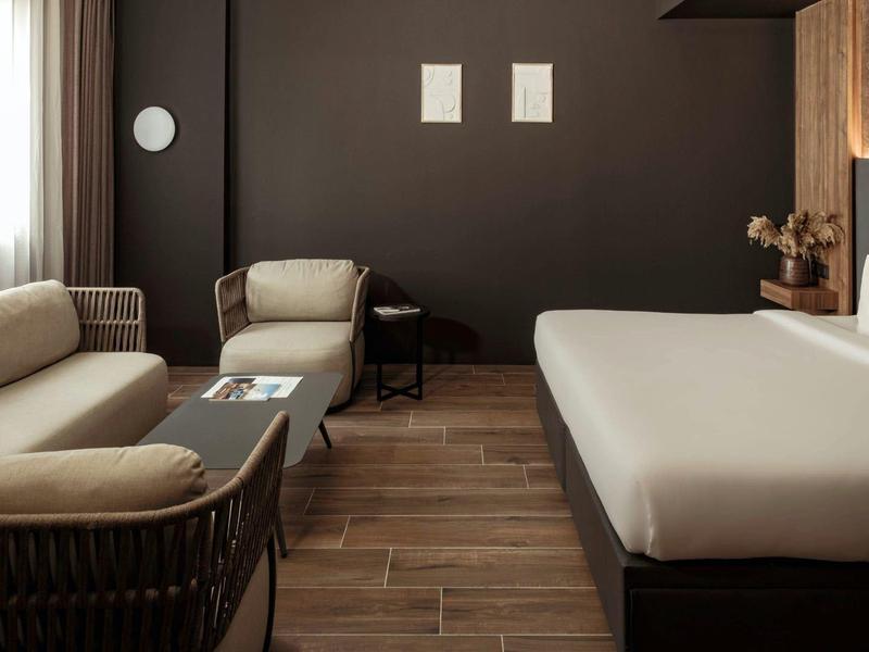 Modernes Hotelzimmer mit bequemen Sitzmöbeln, großem Bett und dunkler Wandgestaltung.