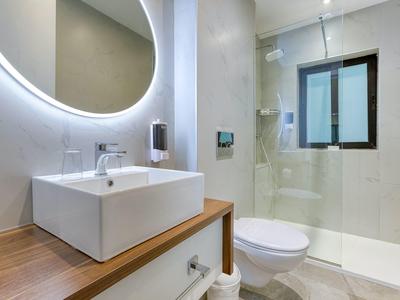 Moderne badkamer met verlichte spiegel, wastafel, toilet en douchecabine met raam.