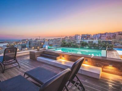 Dachterrasse mit Pool und Stadtblick bei Sonnenuntergang in einem Hotel.