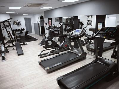 Moderne Fitnessstudio mit Laufbändern, Fahrrädern und diversen Trainingsgeräten in einem hellen Raum.