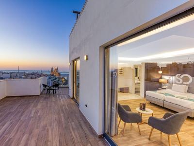 Moderner Hotelbalkon mit Sitzbereich und Blick auf die Stadt bei Sonnenuntergang.