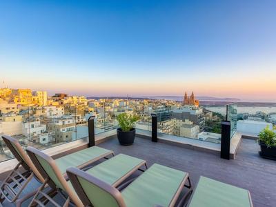 Dachterrasse mit Liegen und Blick auf eine Stadt bei Sonnenuntergang.