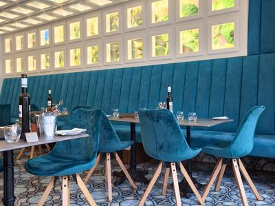 Moderner Essbereich mit blauen gepolsterten Stühlen und Holztischen neben einer Glasfensterwand.