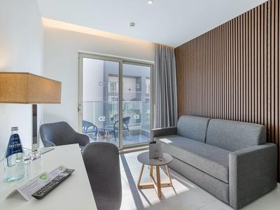 Modern ingerichte hotelkamer met grijze bank, bureau en groot raam.
