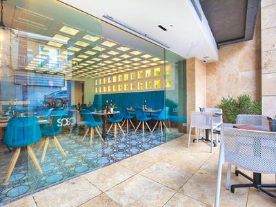 Moderne buitenruimte van een café met blauwgroene stoelen en glazen wand.