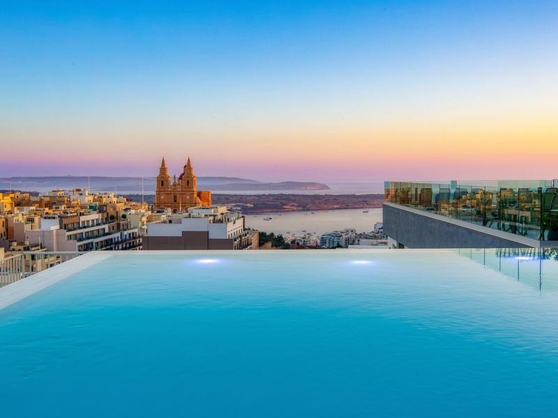 Dakterraszwembad met uitzicht op stad, kathedraal en zee bij zonsondergang.