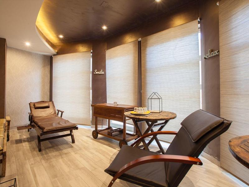 Lichte, moderne kamer met comfortabele ligstoelen en houten tafels bij grote ramen met jaloezieën.