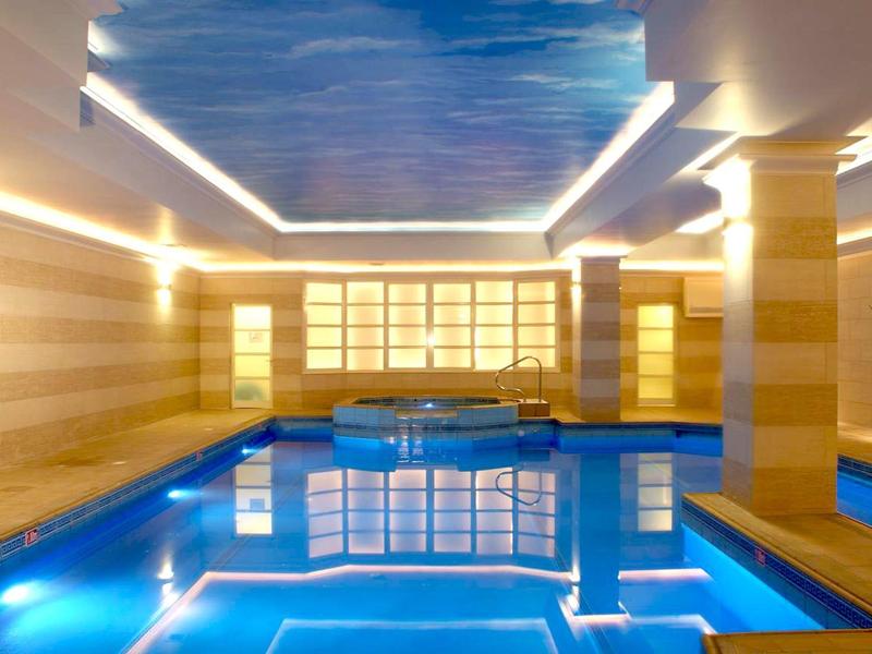 Modern binnenzwembad met blauwe tegels en indirecte verlichting aan het plafond.