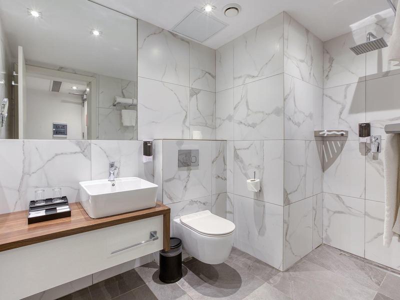 Moderne badkamer met witte tegels en houten meubels in een hotelkamer.