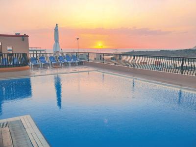 Ein ruhiger Pool mit Sonnenliegen und Blick auf den Sonnenuntergang über dem Meer.