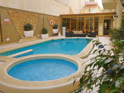 Piscina de hotel con una pequeña piscina redonda para niños y una piscina rectangular más grande en un patio interior.