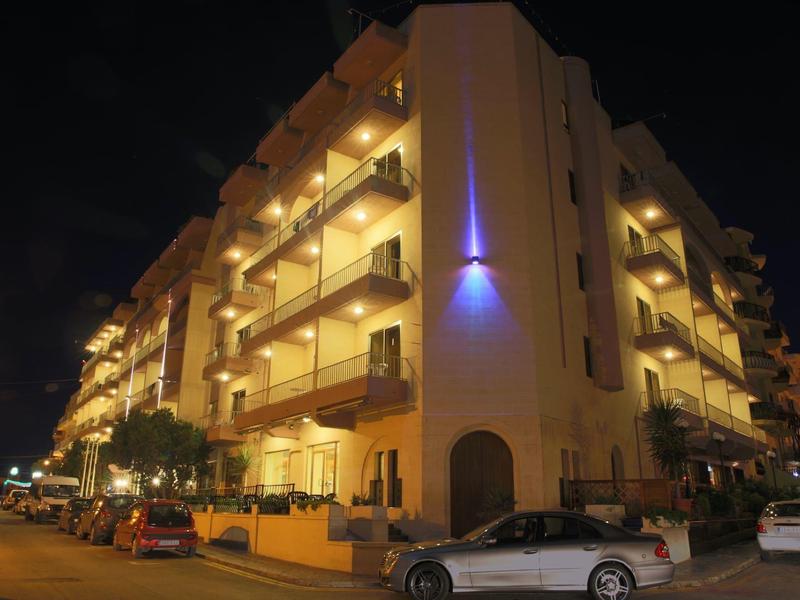 Osvětlená vícepatrová hotelová budova s balkony a zaparkovanými auty v noci