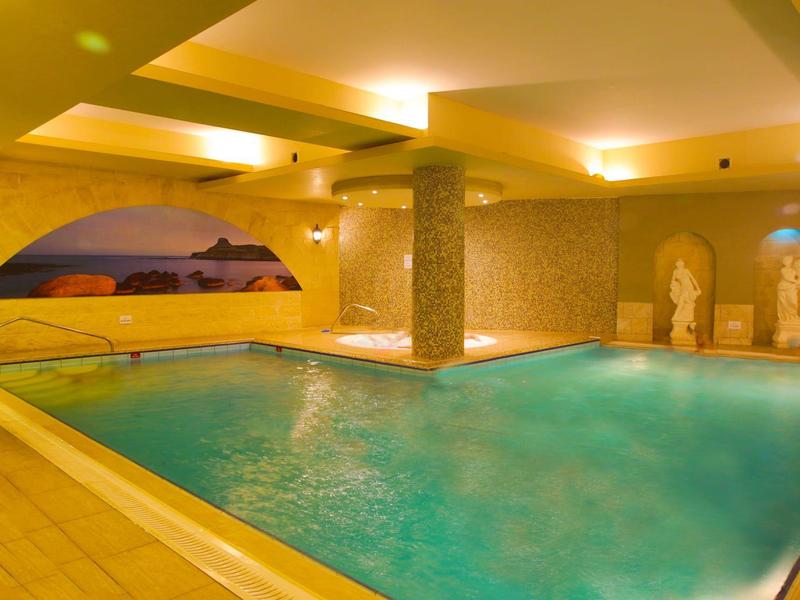 Vnitřní hotelový bazén s teplým osvětlením, dekorativními sloupy a nástěnnými malbami