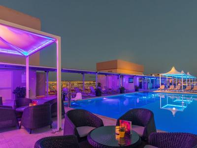Terraza en la azotea con piscina iluminada y zonas de estar al anochecer