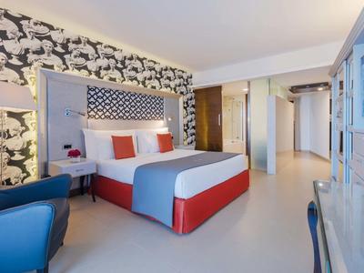 Nowoczesny pokój hotelowy z dużym łóżkiem, wzorzystą ścianą i niebieskim fotelem.