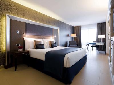 Nowoczesny pokój hotelowy z dużym łóżkiem, biurkiem i oknem z zasłonami.