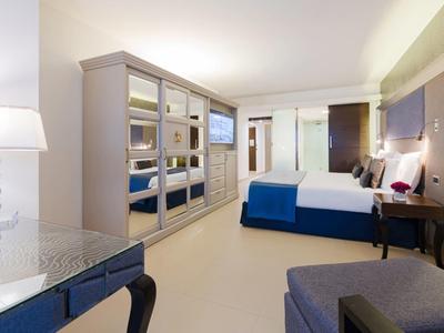 Nowoczesny pokój hotelowy z dużym łóżkiem, niebieskimi akcentami i lustrzanymi szafami.