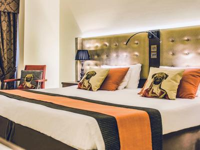 Elegantes Hotelzimmer mit zwei Betten, orangen Akzenten und bequemen Kissen.