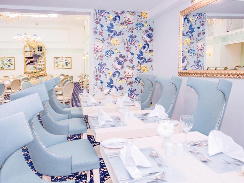 Elegantes Restaurant mit blauen Sesseln und floralem Wanddesign