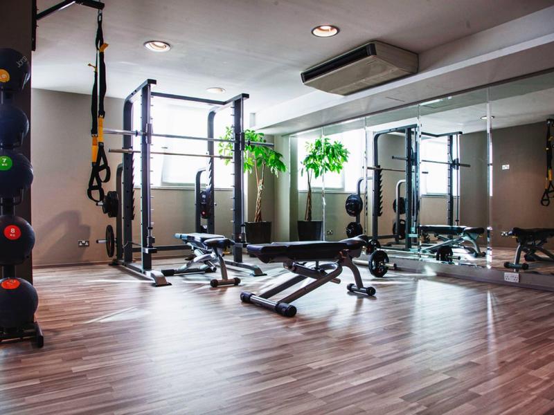 Moderner Fitnessraum mit Trainingsgeräten, Spiegelwand und Holzfußboden in einem Hotel.