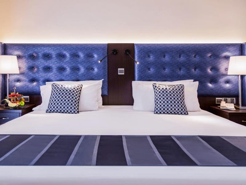 Modernes Doppelbett mit gepolstertem blauem Kopfteil und dekorativen Kissen.