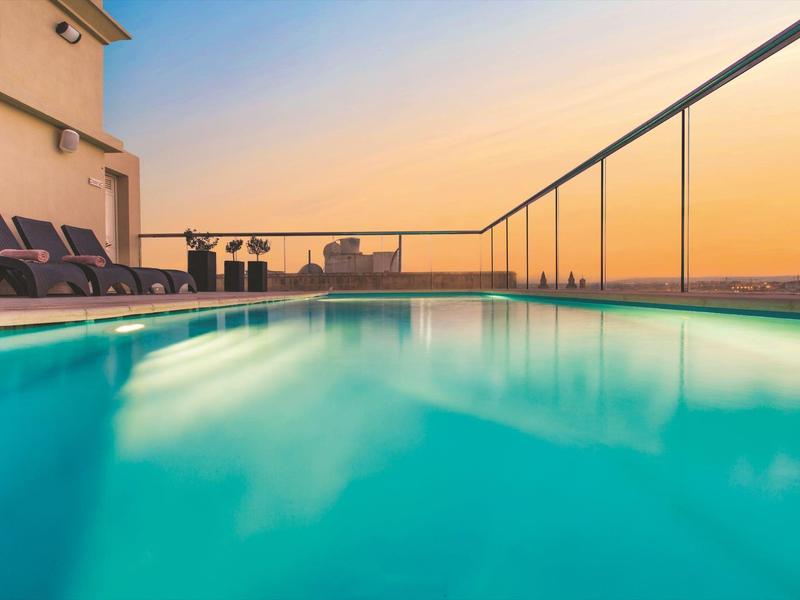 Dachpool mit Liegestühlen und Glasgeländer bei Sonnenuntergang.