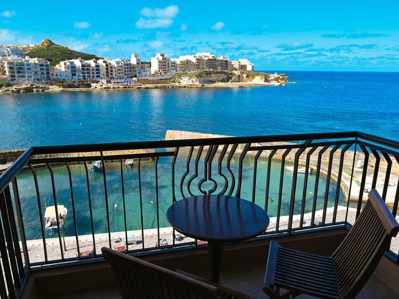 Balcony with table and chair overlooking the sea and coastal hotel.