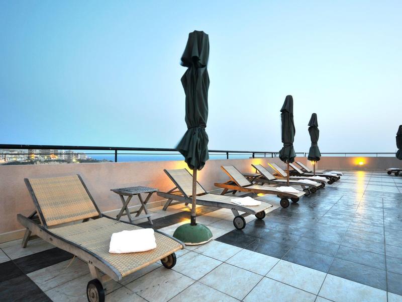 Empty lounge chairs with closed umbrellas on a rooftop terrace at sunset