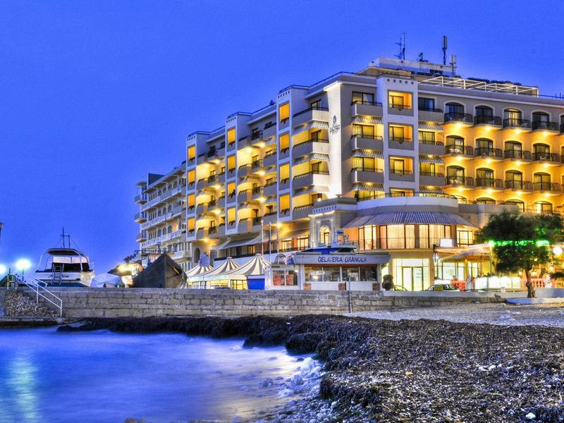 Illuminated hotel building on the shore with pebble beach and calm sea at night