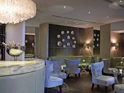 Elegante Hotellounge mit hellblauen Sesseln, runden Tischen und einer Bar mit Marmorplatte.