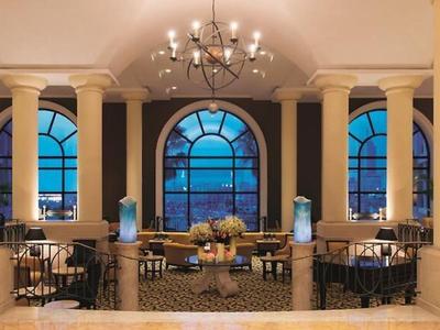 Elegante hotel eetkamer met kroonluchter, bogen ramen en zeezicht bij schemering.