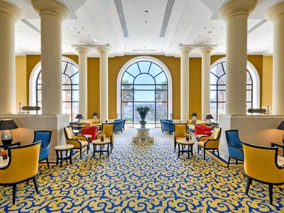 Eleganter Hotel-Loungebereich mit gelben Sesseln, blauen Kissen und großen Fensterbögen