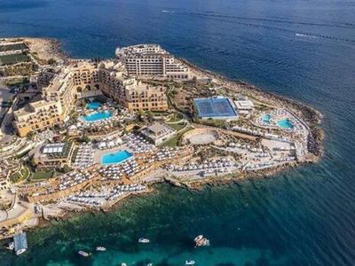 Luchtfoto van een kustresort met zwembaden, gebouwen en strand langs de heldere blauwe zee.
