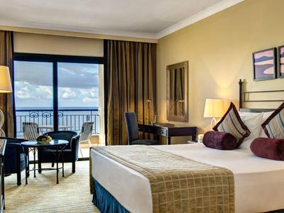 Hotelkamer met groot bed, zithoek en balkon met uitzicht op de zee.