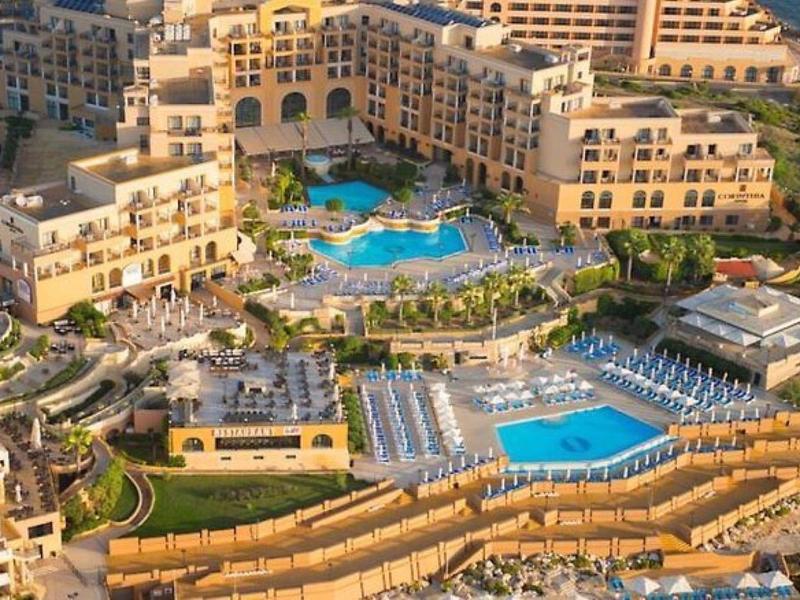 Luchtfoto van een groot resort met meerdere zwembaden, ligbedden en beige gebouwen aan de kust.