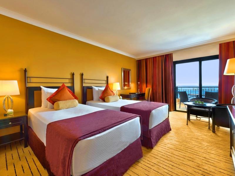 Hotelkamer met twee bedden, oranje muren en een balkon met uitzicht op zee.