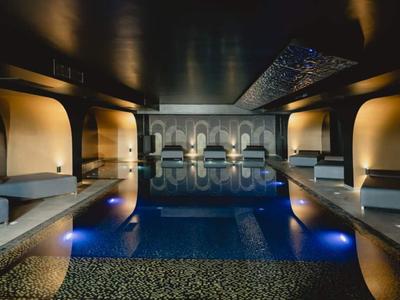 Piscina interna di lusso con illuminazione soffusa e decorazioni murali ornate.
